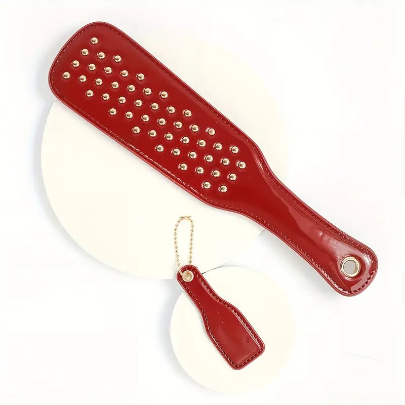 deze-glanzend-rode-paddel-is-een-leuke-instapper-voor-je-bdsm-spel-of-een-leuke-bdsm-toy-aanvulling-op-je-reeds-bestaande-assortiment-met-zijn-tientallen-vergulden-studskomt-hij-net-weer-iets-anders-aan-dan-je-andere-paddels-2