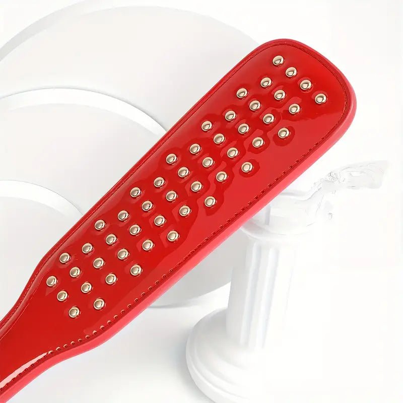 deze-glanzend-rode-paddel-is-een-leuke-instapper-voor-je-bdsm-spel-of-een-leuke-bdsm-toy-aanvulling-op-je-reeds-bestaande-assortiment-met-zijn-tientallen-vergulden-studskomt-hij-net-weer-iets-anders-aan-dan-je-andere-paddels-5